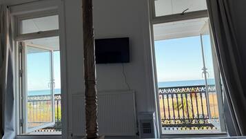 A room with a bed, a television, and large windows with a view of the sea.