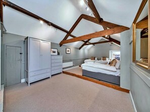 Ein Schlafzimmer mit schrägem Dach, einem Kleiderschrank, einem Bett mit Kissen und einem Fenster.