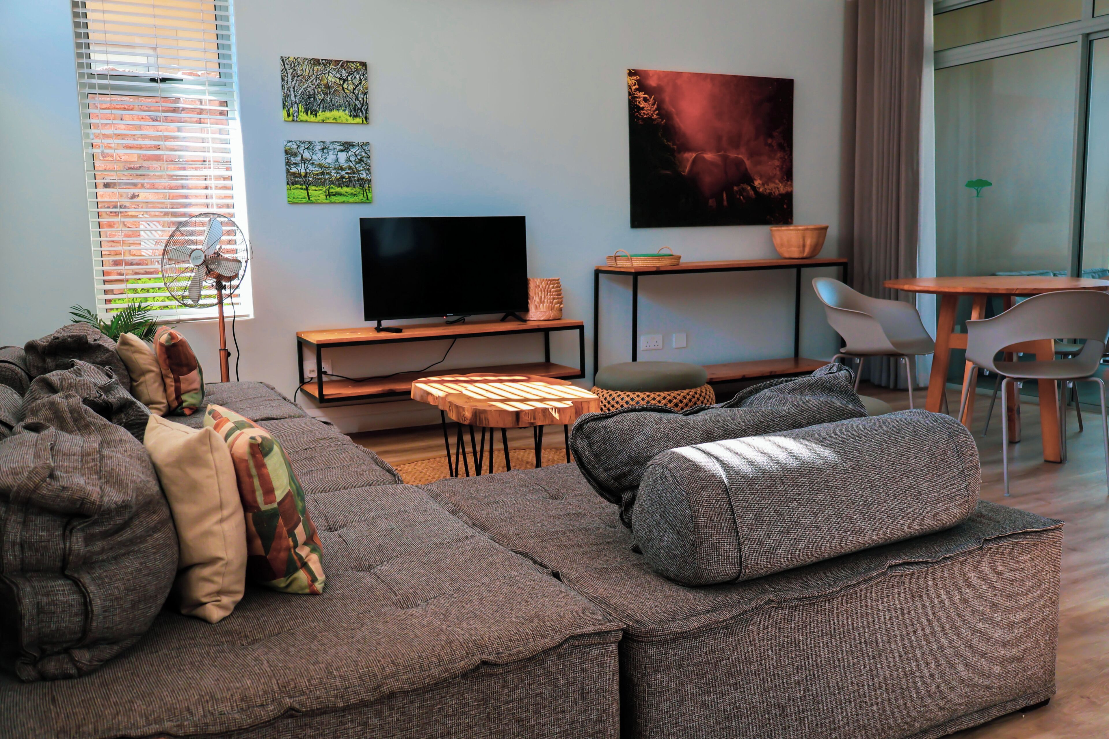 Een moderne woonkamer met een hoekbank, een flatscreen-tv, een klein houten tafeltje en een eethoek met stoelen.