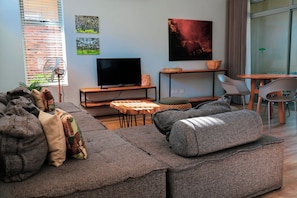 Una sala de estar moderna con un sofá modular, un televisor de pantalla plana, una mesita de madera y un comedor con sillas.