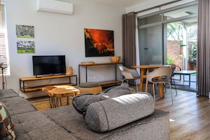 Una sala de estar moderna con un televisor de pantalla plana, un sofá, una mesa de centro y un comedor con sillas.