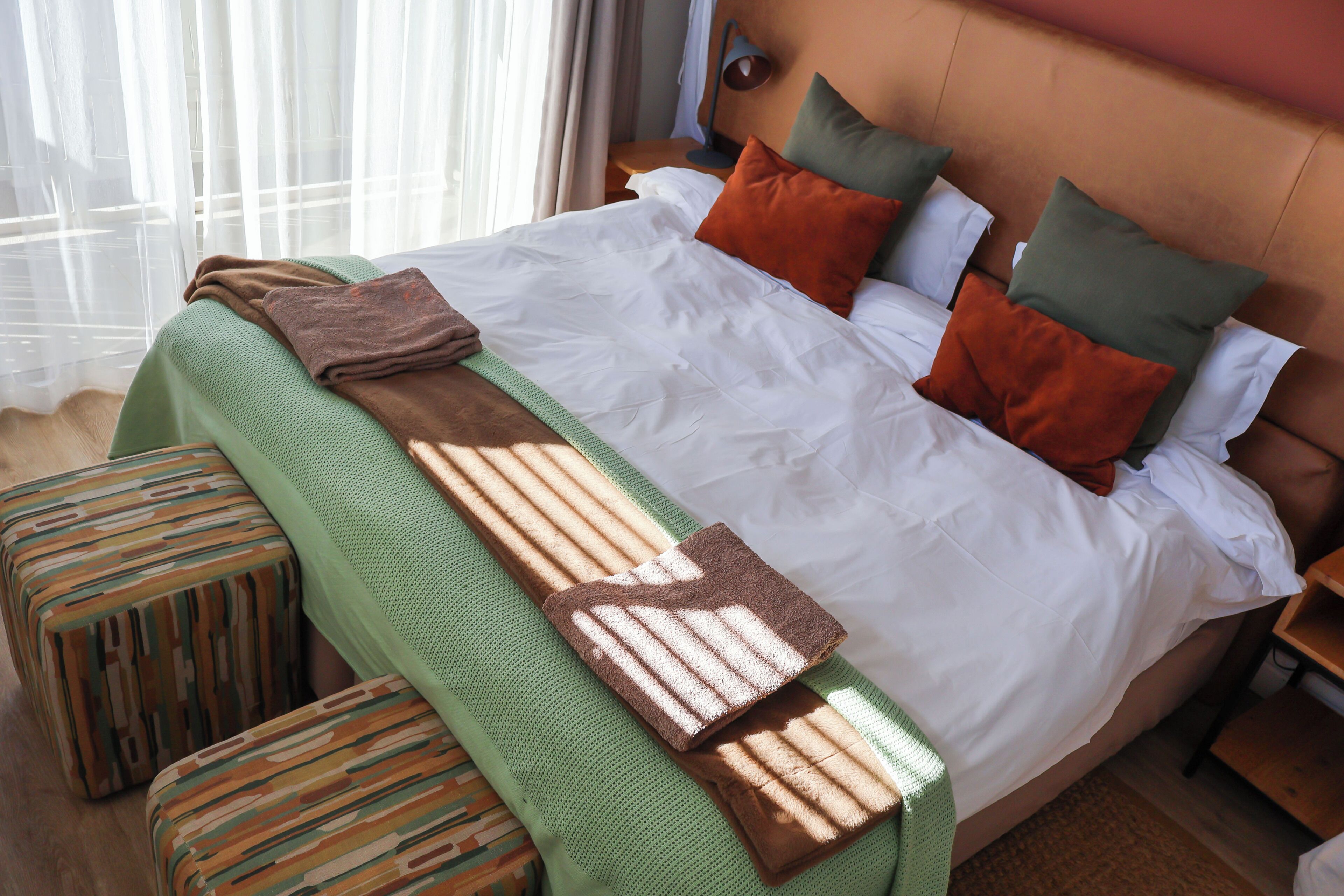 Un letto rifatto con cura, una coperta verde e una trapunta marrone, una panca in legno e un comodino con una lampada.