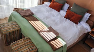 Un letto rifatto con cura, una coperta verde e una trapunta marrone, una panca in legno e un comodino con una lampada.