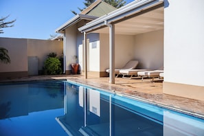 A swimming pool with a sunlit patio area, lounge chairs, and a covered seating area.