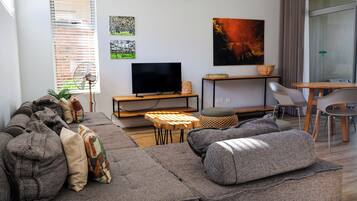 A modern living room with a sectional sofa, a flat-screen TV, and a dining area with a table and chairs.