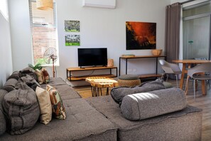 Una sala moderna con un sofá modular, un televisor de pantalla plana y un comedor con mesa y sillas.