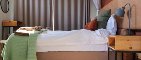 A neatly made bed with a white comforter and pillows, a bedside lamp, and a wooden nightstand with a lamp.