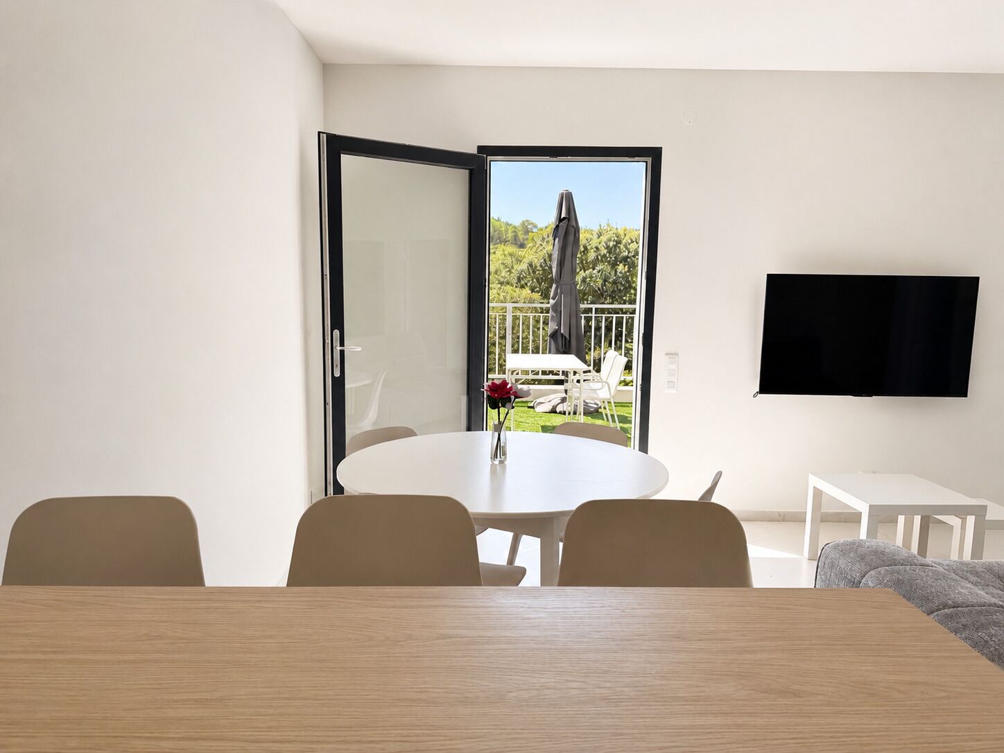 Een moderne woonkamer met een ronde tafel, een flatscreen televisie aan de muur en een balkon met tuinmeubilair.