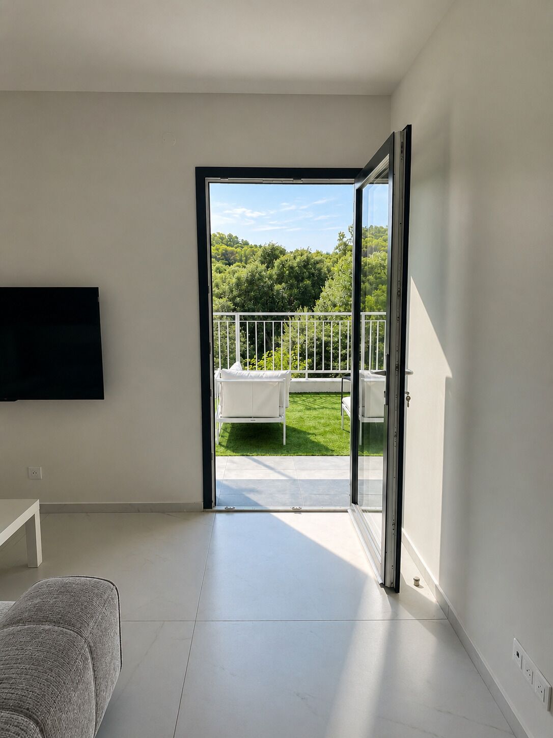 Un intérieur moderne avec une porte-fenêtre coulissante donnant sur un patio extérieur agrémenté d’une table et de chaises blanches.