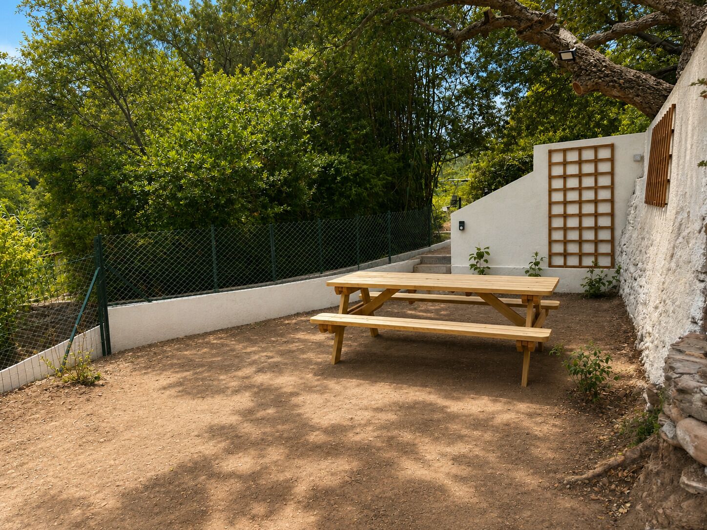 A picnic table in a garden area with a white wall and a wooden fence.
