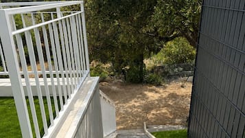 Un escalier menant à une zone abritée, dotée d’une rambarde blanche, et entouré d’une pelouse verdoyante et d’un arbre.