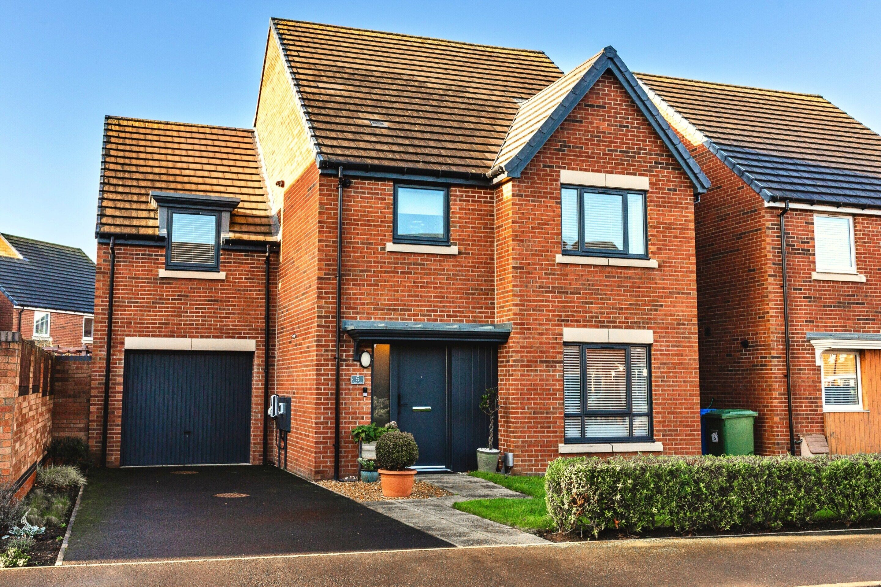 A two-story brick house with a front garage, a small front yard, and a clear sky.