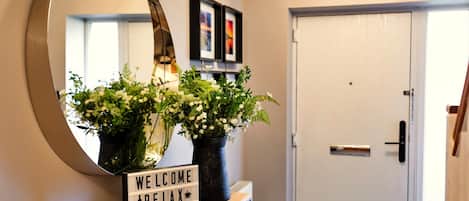 A reception area with a mirror, a welcome sign, and two flower arrangements on a wooden counter.