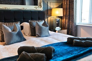 A hotel room with a large bed, multiple pillows, a bedside table with a lamp, and a window with curtains. - Beach House Near Northumberland' (Blyth)