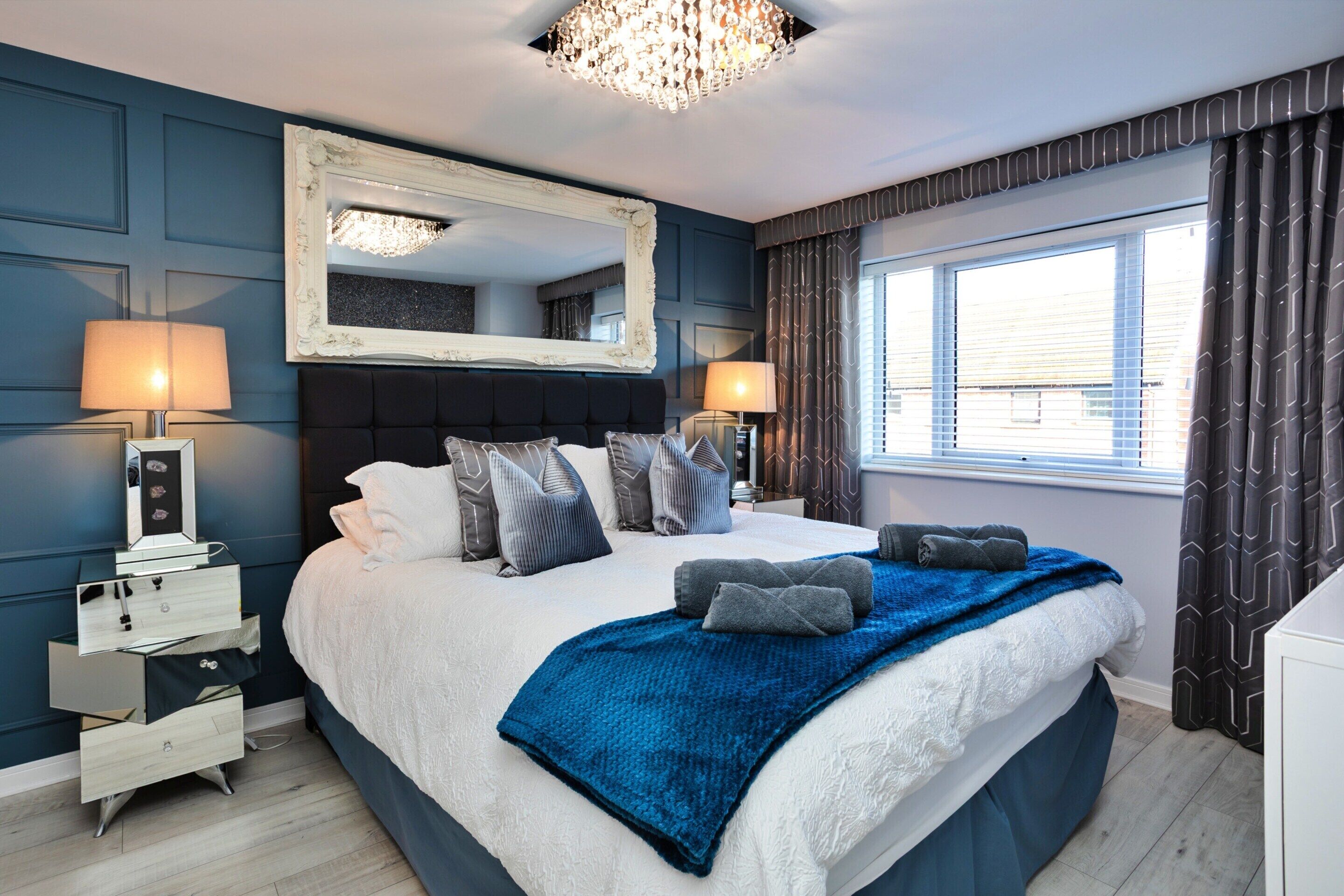 A hotel bedroom with a large bed, bedside lamps, a mirror, and a window with curtains.