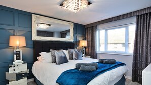 Ein Hotelzimmer mit einem großen Bett, Nachttischlampen, einem Spiegel und einem Fenster mit Vorhängen.