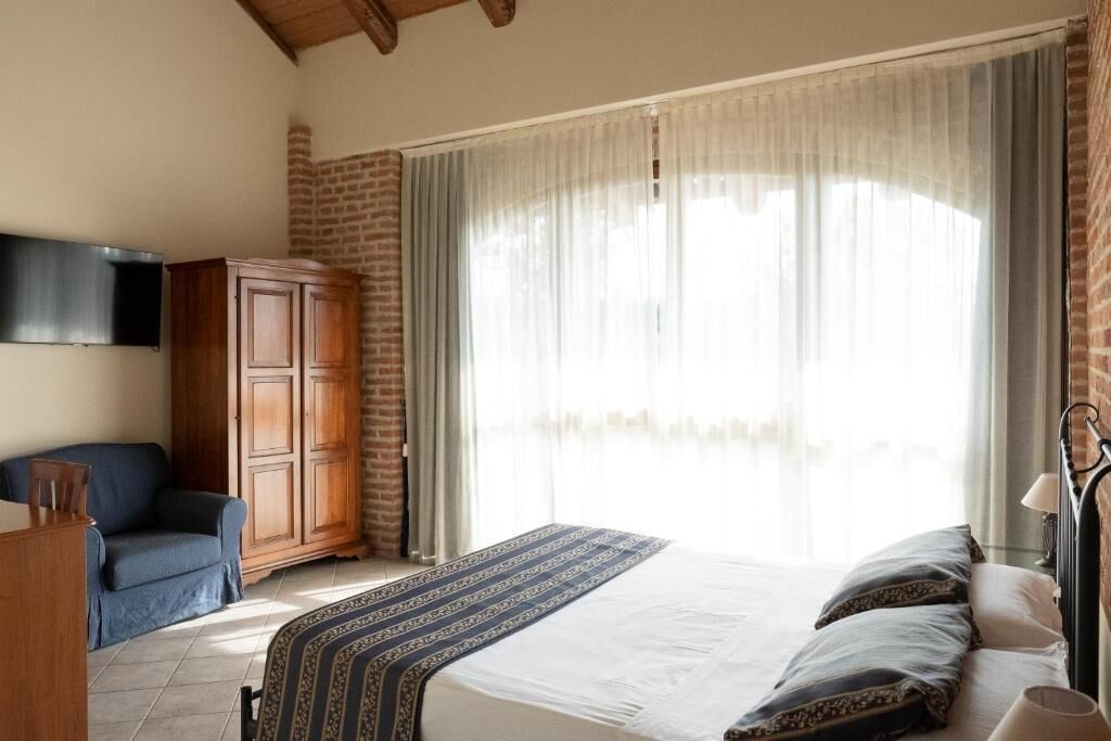 A bedroom with a bed, a wooden wardrobe, a television, and a window with curtains.