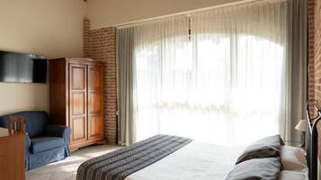 A bedroom with a bed, a wooden wardrobe, a television, and a window with curtains.