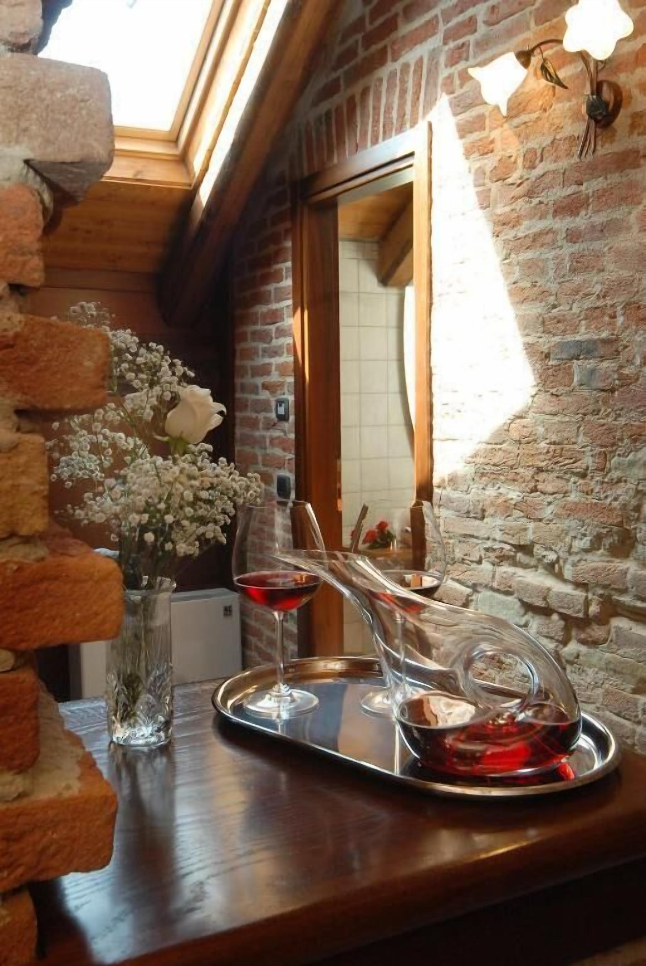 Una mesa de madera con una bandeja que sostiene dos copas de vino tinto y un florero con flores blancas.