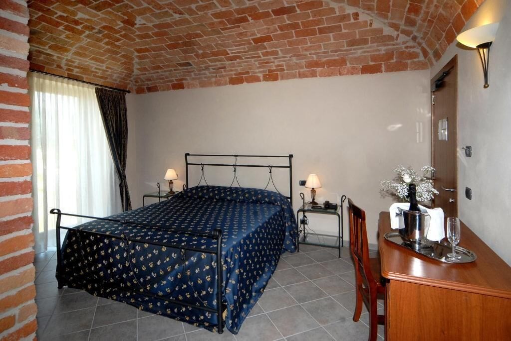 Una habitació amb un llit, taules de nit, un escriptori de fusta i un sostre de rajola.