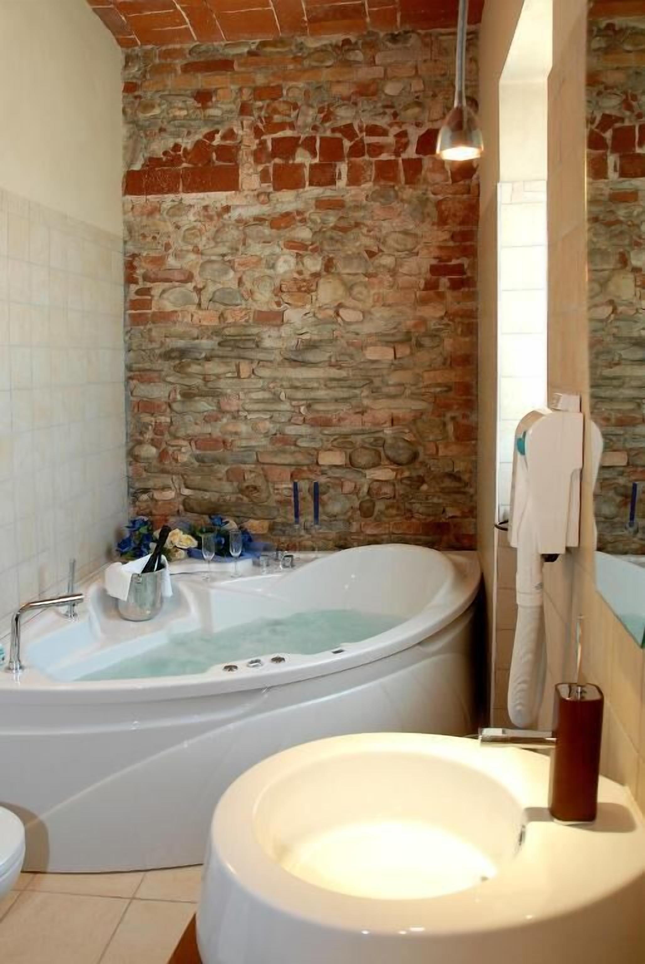 Un baño con pared de piedra, una bañera, un lavamanos y un espejo.