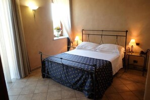 A hotel room with a bed, two bedside lamps, a window with curtains, and a wall-mounted light fixture. - HOTEL LE BOTTI (Guarene)