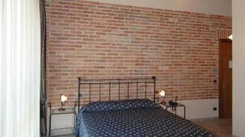 Een slaapkamer met een bakstenen muur, een bed met een geborduurde spreideken, een houten plafond en een wandlamp.