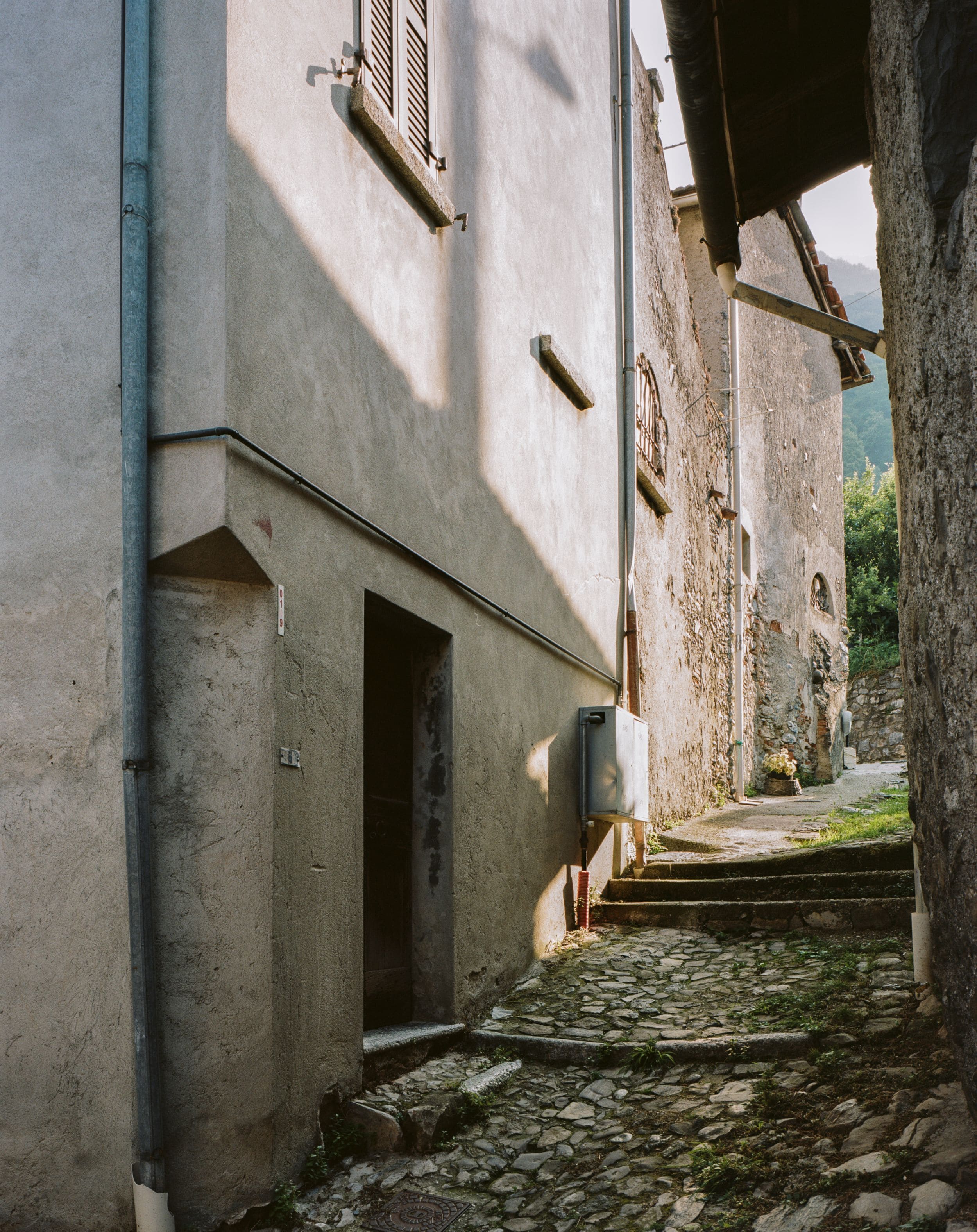 A narrow cobblestone street flanked by buildings with stone walls and wooden shutters.