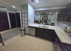 A modern kitchen with dark cabinets, a granite countertop, and a tiled floor. - Amazing Oceanfront With Access Crocs Resort (Jacó)