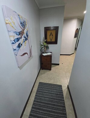 A hallway with a decorative wall piece, a small wooden cabinet with a vase, and a patterned rug. - Amazing Oceanfront With Access Crocs Resort (Jacó)
