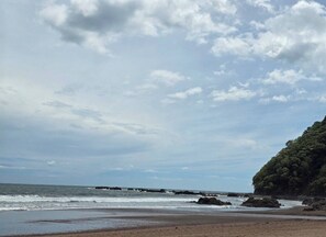 A beach with waves, a rocky shoreline, and a forested cliff. - Amazing Oceanfront With Access Crocs Resort (Jacó)