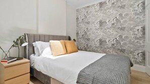 A bedroom with a bed, bedside table, and a wall with a textured pattern. - 44 Adelaide Street (Surry Hills)