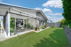 A modern house with a covered patio, a lawn, and a variety of potted plants. - Corlette Coastal Haven (Corlette)