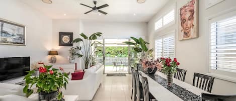 A modern interior with a dining area, white sofas, a TV, and various plants.