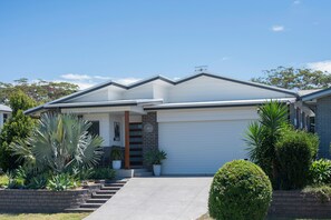 A modern two-story house with a garage, surrounded by well-maintained landscaping including palm trees and shrubs. - Corlette Coastal Haven (Corlette)