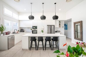 A modern kitchen with a central island, bar stools, a refrigerator, and pendant lights. - Corlette Coastal Haven (Corlette)