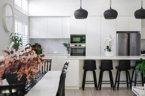 A modern kitchen with white cabinetry, a central island, black bar stools, and pendant lighting. - Corlette Coastal Haven (Corlette)