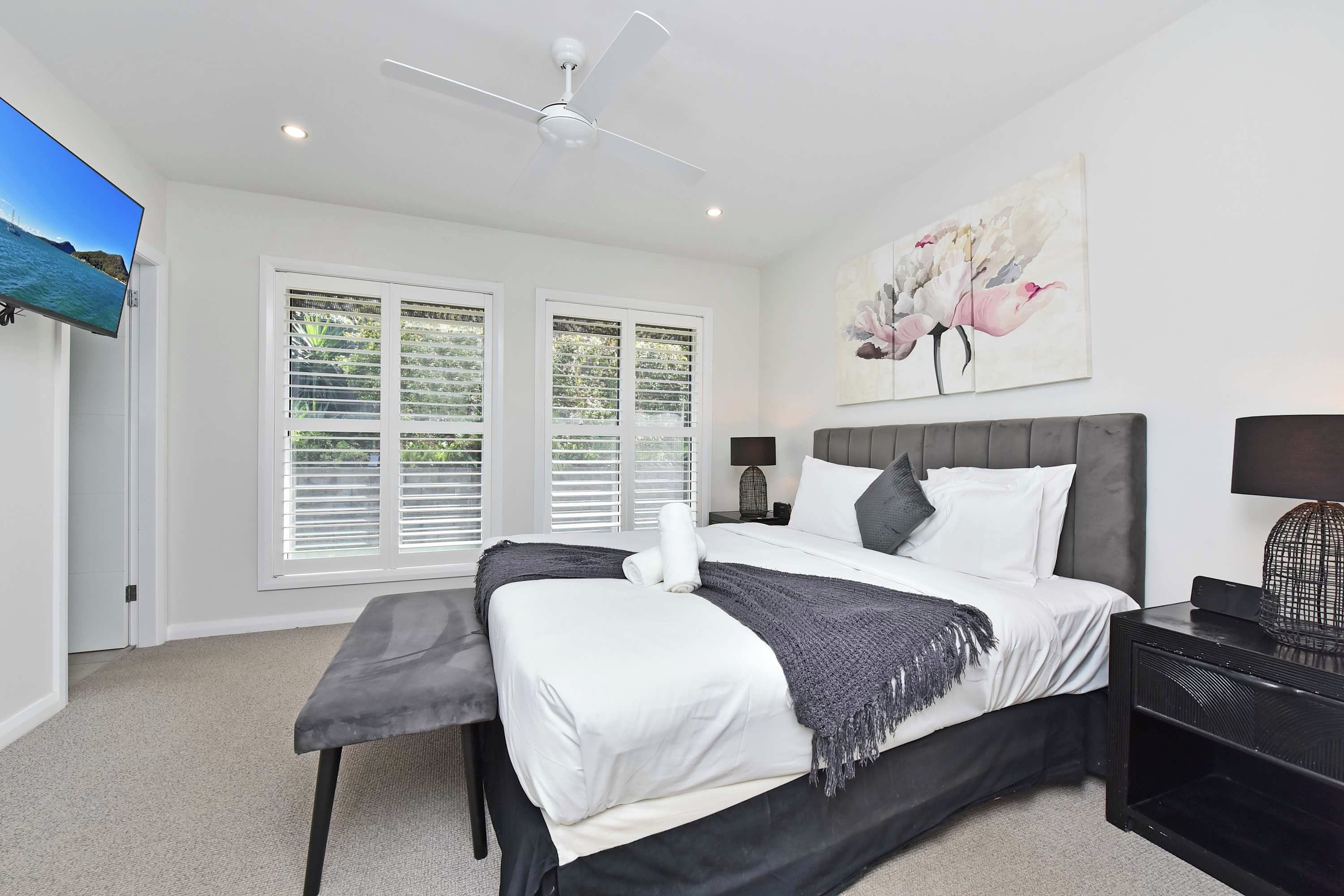 A bedroom with a bed, a ceiling fan, a TV, and a painting.