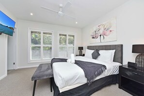 A bedroom with a bed, a ceiling fan, a TV, and a painting. - Corlette Coastal Haven (Corlette)
