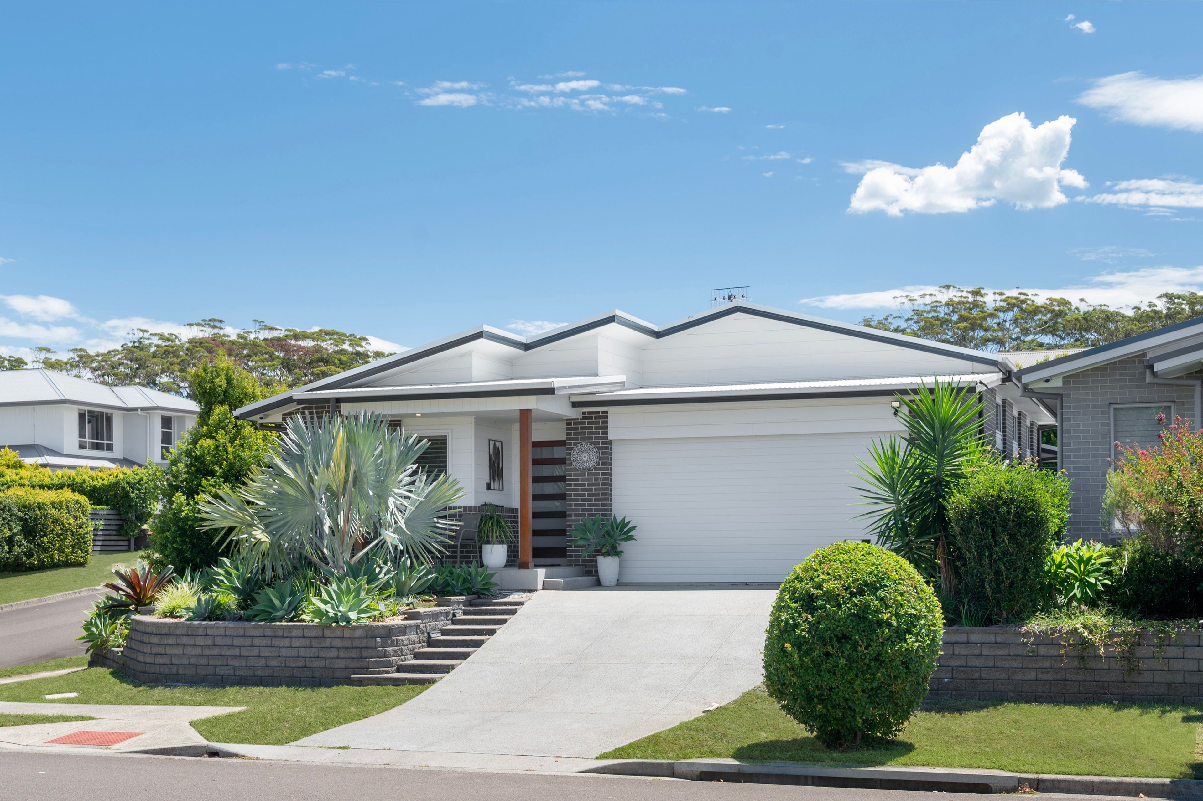 A residential house with a garage, a front yard with various plants, and a clear blue sky.