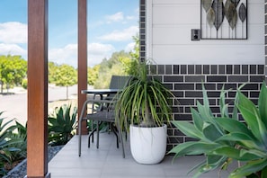 A patio area with a table and chairs, a potted plant, and a wall-mounted decorative element. - Corlette Coastal Haven (Corlette)
