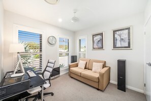 A modern office space with a desk, chair, and a beige sofa. There are two framed artworks on the wall and a clock. - Corlette Coastal Haven (Corlette)
