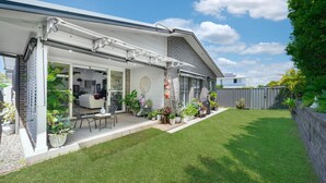 A modern house with a covered patio, a lawn, and a fenced backyard. - Corlette Coastal Haven (Corlette)