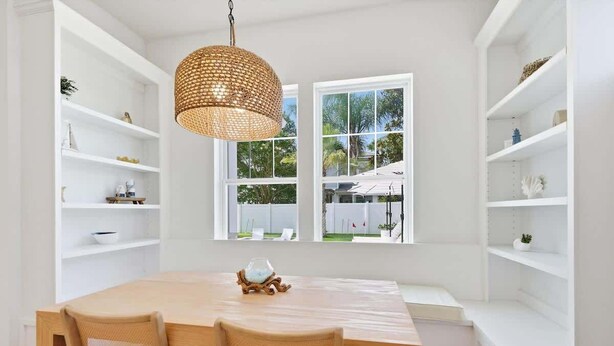 A dining area with a wooden table and chairs, white shelving units, and a large window with a view of greenery. - NEW! Large Luxury Beach Villa: Heated Pool Oasis (Jacksonville Beach)
