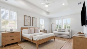 A modern bedroom with a wooden bed, bedside tables, a sofa, and a TV. - NEW! Large Luxury Beach Villa: Heated Pool Oasis (Jacksonville Beach)