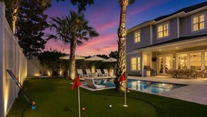 A backyard with a swimming pool, a putting green, and a patio area with outdoor furniture. - NEW! Large Luxury Beach Villa: Heated Pool Oasis (Jacksonville Beach)