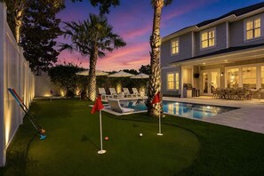A backyard with a swimming pool, a putting green, and a patio area with outdoor furniture.