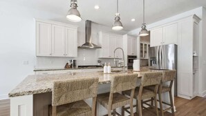 A modern kitchen with white cabinets, a granite countertop, and a stainless steel refrigerator. - NEW! Large Luxury Beach Villa: Heated Pool Oasis (Jacksonville Beach)
