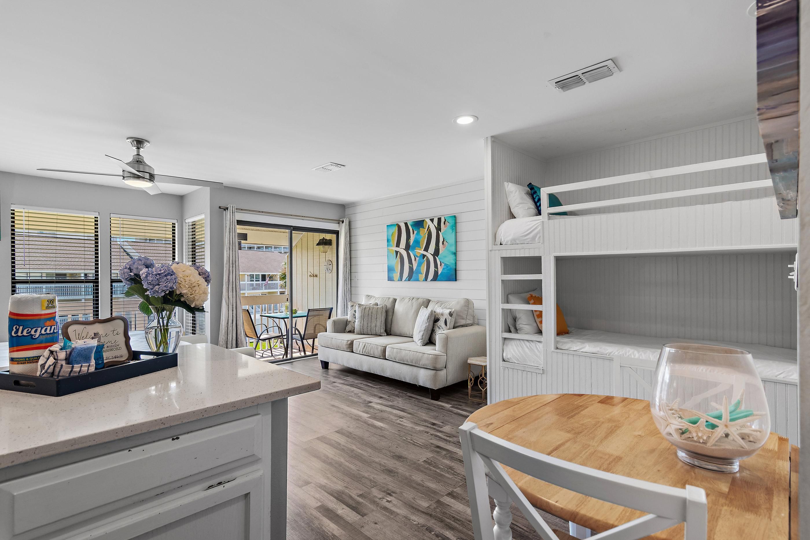 A modern kitchen with a dining area, a white sofa, and a bunk bed with storage.