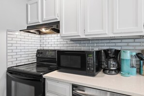 A kitchen with white cabinets, a black stove, a microwave, and a coffee maker. - Sandpiper Cove 8242 (Destin)